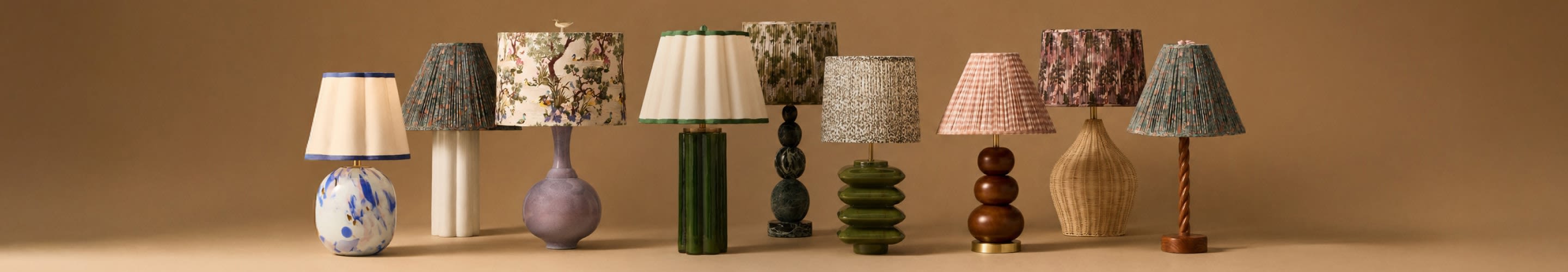 Collection of decorative table lamps with various patterned shades and bases in different shapes and colors against a tan background.