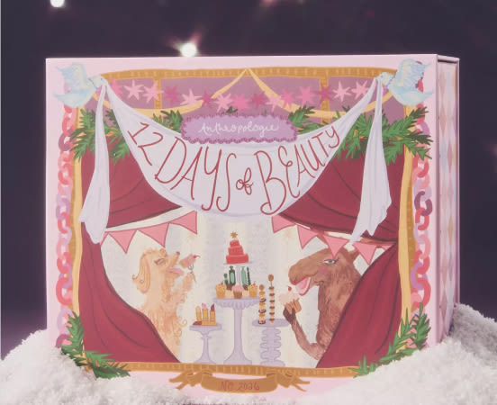 Open book displaying illustrated cover with "12 Days of Beauty" text, red curtains, unicorns, and festive decorations on white snow.