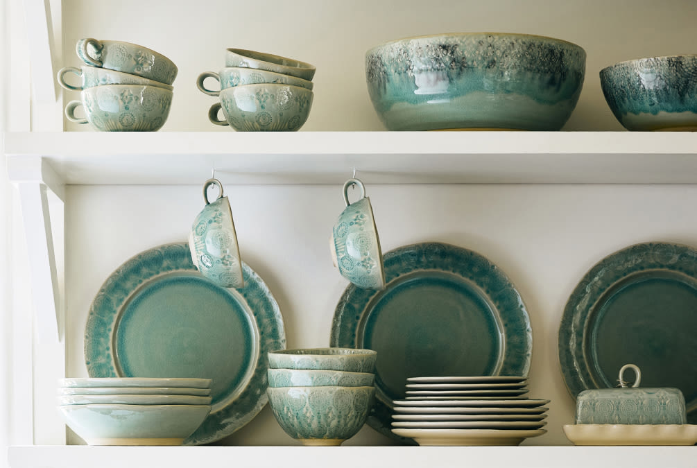 White shelves displaying turquoise and cream ceramic dinnerware including plates, bowls, cups, and serving dishes.