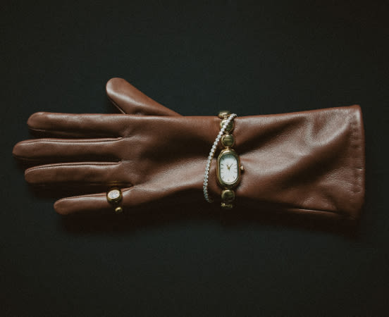 Brown leather glove with gold watch and ring on dark background