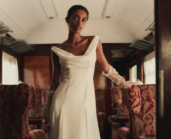 Woman in elegant white wedding gown with draped neckline in vintage train car. Text reads "HERE'S TO THE HAPPY COUPLE"