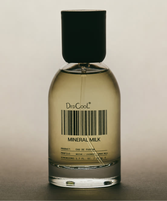 Perfume bottle with golden liquid and black cap labeled DedCool MINERAL MILK with barcode on beige background