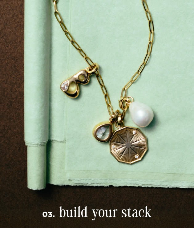 Gold chain necklace with pearl and charm pendants on mint green notebook with text "03. build your stack"