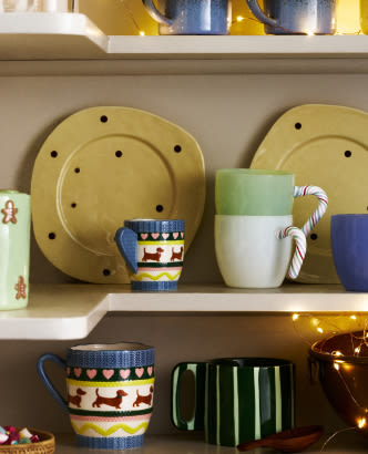 White shelves displaying colorful dishware including yellow polka dot plates, blue patterned mugs, a candy cane mug, and a green striped cup.