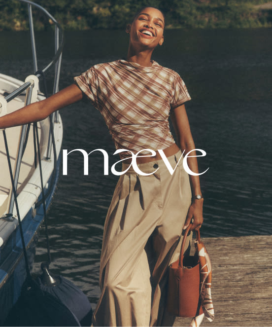 Woman in striped brown shirt and beige pants laughing on dock by boat with water behind her, text reads maeve