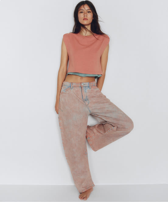 Woman wearing coral sleeveless crop top and high-waisted beige wide-leg jeans against white background