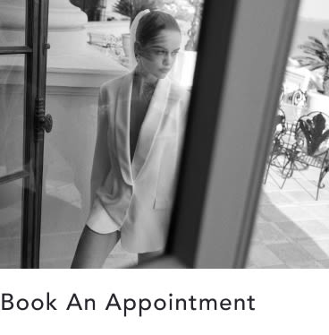 Black and white photo of woman in blazer and sunglasses standing in doorway. Text reads "Book An Appointment"