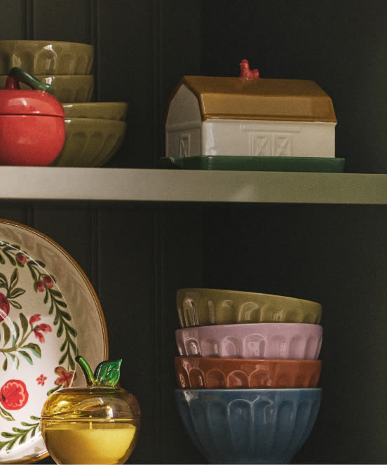 Shelves displaying vintage kitchenware including colorful bowls, a ceramic barn container, floral plate, and golden apple-shaped jar.