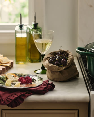 Mediterranean appetizer spread with olives, cheese, crackers, olive oil bottles, and white wine on a kitchen counter.