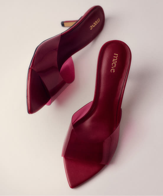Pair of burgundy satin mule heels with pointed toes and crisscross straps, branded "mecie" on insole, on beige background.
