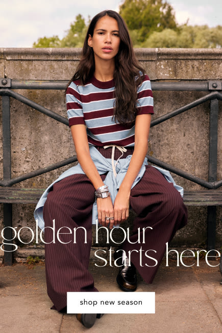 Woman in burgundy and white striped shirt and wide-leg pants sitting outdoors. Text reads "golden hour starts here shop new season"