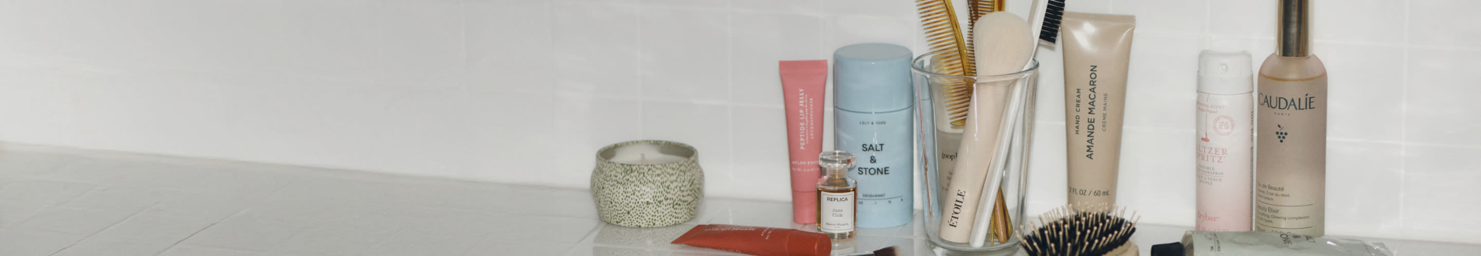 Bathroom counter with beauty products including Salt & Stone deodorant, Caudalie spray, hairbrushes in holder, and skincare items.
