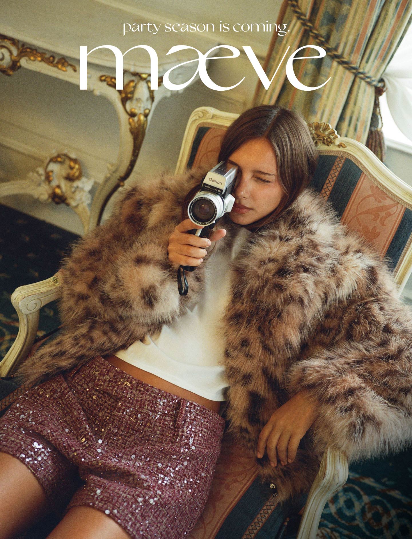 Woman in fur coat and pink sequin skirt holding vintage camera on ornate chair. Text reads party season is coming maeve.