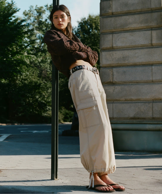 Woman in brown crop top and beige cargo pants leaning against pole outdoors with text "Clothing" overlaid on image.