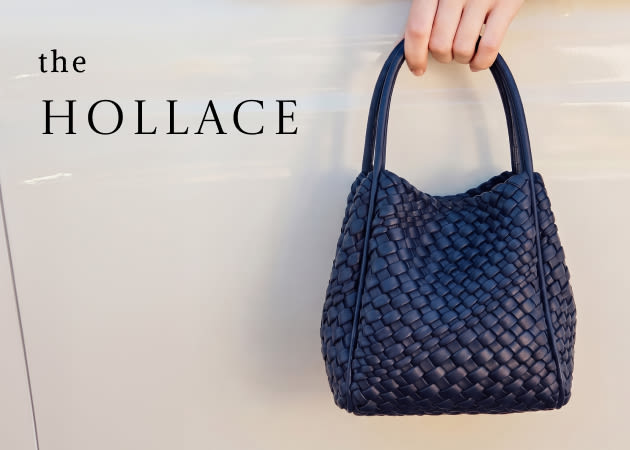 Hand holding a navy blue woven leather handbag with text "the HOLLACE" on light background