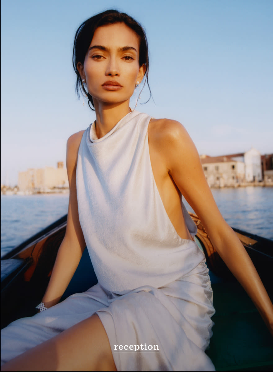 Woman in white sleeveless dress sitting in boat on blue water with coastal buildings in background, text reads reception