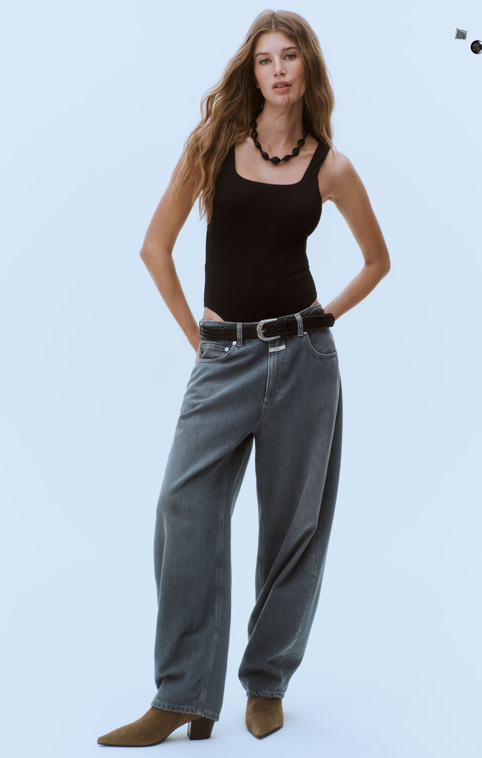 Woman wearing black tank top, black beaded necklace, gray wide-leg jeans with black belt, and brown suede boots.