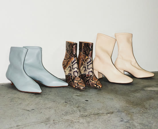 Three pairs of ankle boots in light blue, snakeskin print, and cream displayed on concrete floor against white wall.