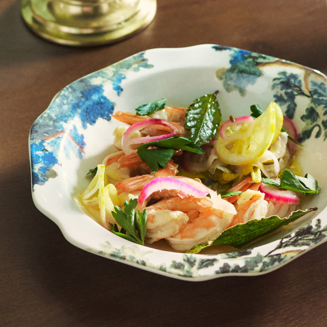 Shrimp salad with pickled onions, herbs, and lemon slices in a decorative blue and white ceramic bowl on a brown table.