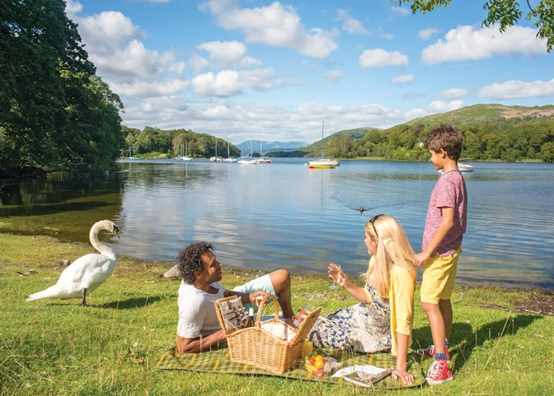 Family enjoying a picnic on the river bank at Crake Valley (CRAK) in Water Yeat, Nr Coniston, The Lake District, Cumbria, England, UK