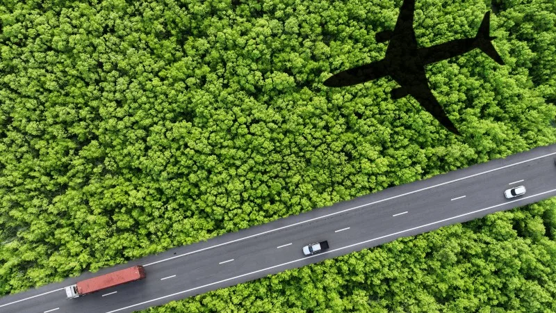 Sustainable transport. Aerial view of eco-friendly vehicles on highway. Electric cars, hydrogen trucks, and SAF-powered airplane shadow over lush green forest.