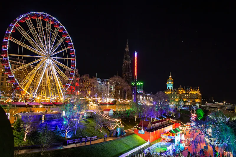 Christmas markets & big wheel lit up at night in Edinburgh city centre, Scotland, UK
