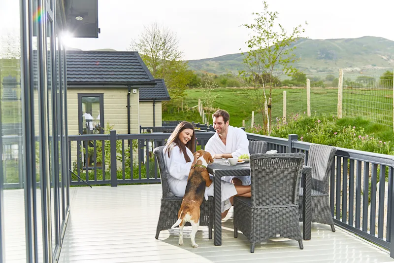 A couple and a dog outside their lodge at Keswick Lodge Retreat in Keswick, Cumbria, The Lake District, England, UK