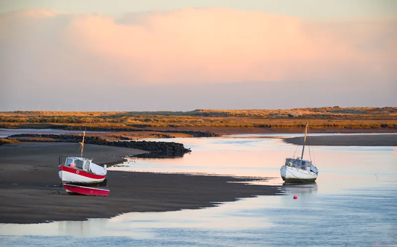 Fishing boats at low tide on the sea creek at Burnham Overy Staithe, Norfolk, at sunrise, England, UK