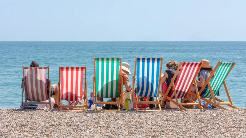 Rear View of Group of People Seated in Six Striped Deckchairs at the Seaside on a Bright Sunny Summer Day
