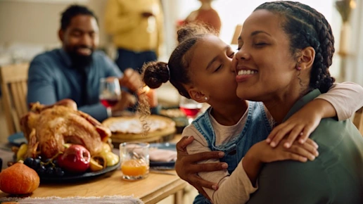 Grateful black girl kisses her mother during family meal.