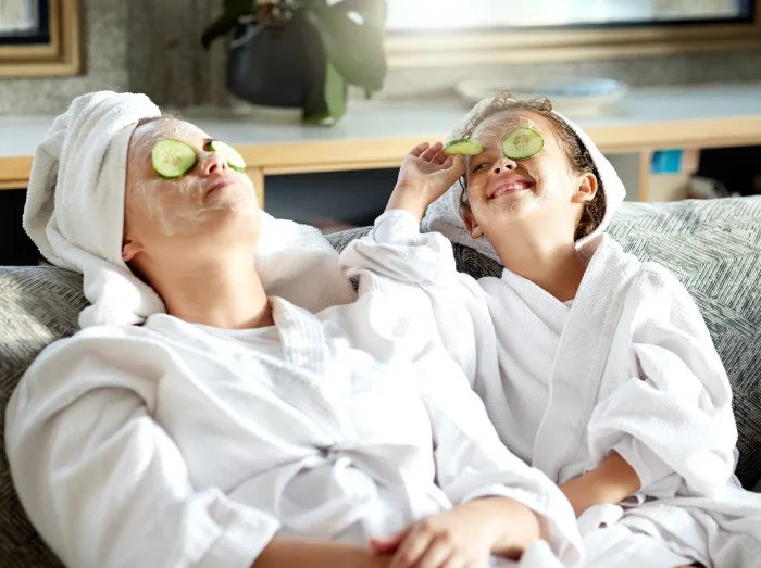 Fresh skincare, face mask and healthy skin treatment for bonding mother and daughter home spa day. Fun, smiling and playful child and parent relaxing with cucumber over their eyes in grooming