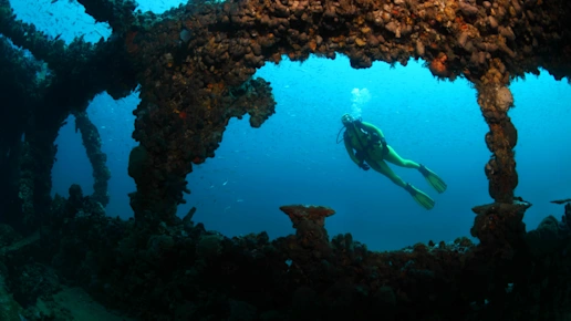 Ein Taucher taucht mit Atemgerät an einem Wrack im Meer.
