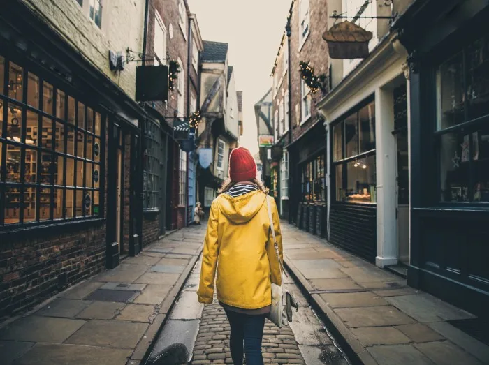 A rear view of a girl in a yellow coat walking along the historic street known as The Shambles in York, UK which is a popular tourist destination and medieval landmark