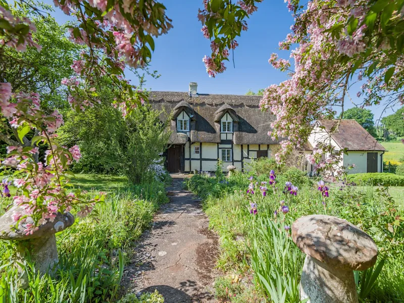 The exterior of Glebe Cottage, with its beautiful garden and thatched roof, in Callow End, Worcester, UK