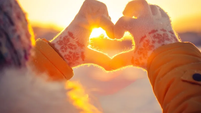 Woman hands in winter gloves Heart symbol shaped Lifestyle and Feelings concept with sunset light nature on background