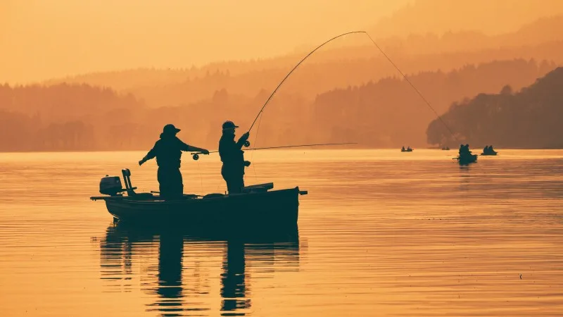 Silhouette of man fishing on lake from boat at sunset. Lake of Menteith, Stirlingshire, Scotland,
