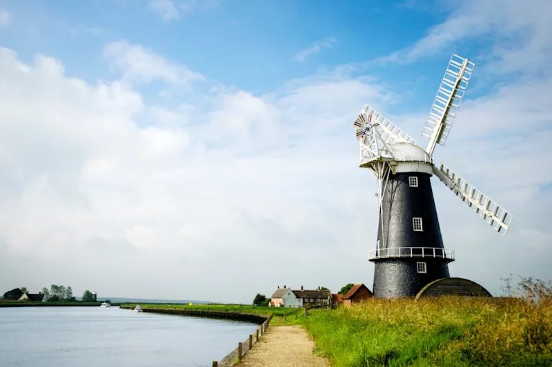 Windmill in the countryside by a river in the Norfolk Broads, England, UK