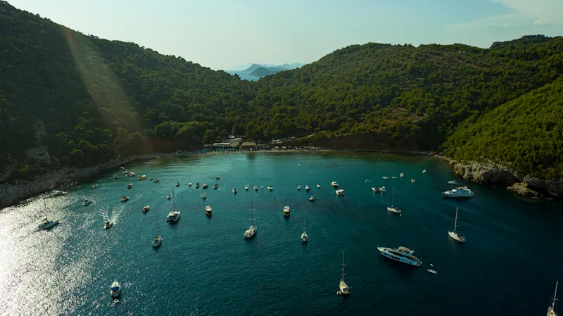 Udsigt over Sunj Beach på øen Lapad, tæt på Dubrovnik i Kroatien. Bugt med skov i baggrunden og både på havet.