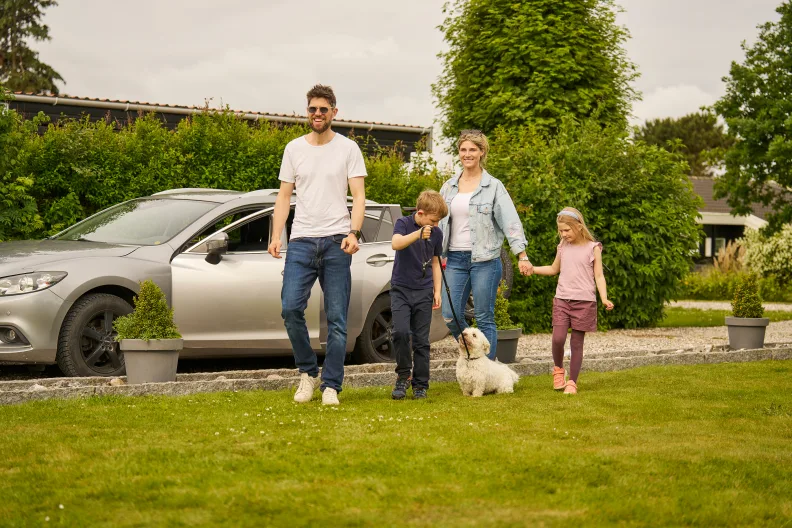 Eine Familie mit zwei Kindern und Hund vor einem silbernen Auto.