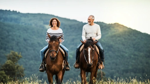 A senior couple riding horses in nature.