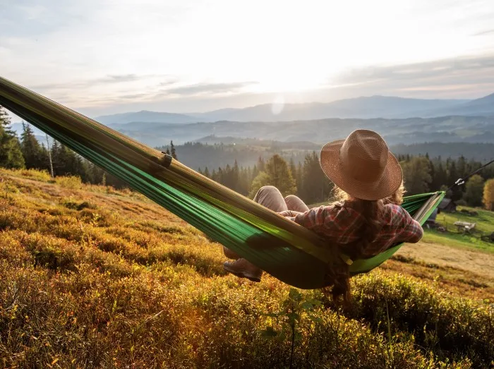 Woman hiker resting after climbing in a hammock at sunset