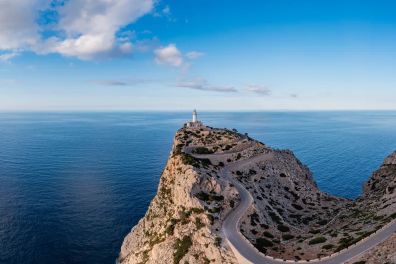 Leuchtturm auf Bergspitze mit Meer im Hintergrund.