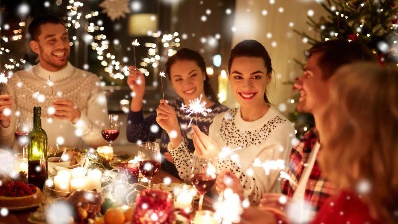 winter holidays and people concept - happy friends with sparklers celebrating christmas at home feast over snow