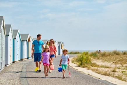 Family walking along a promenade between the beach and a row of colourful beach huts