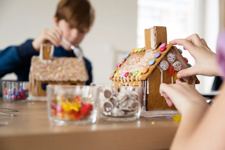 Zwei Kinder verzieren Lebkuchenhäuser mit Süßigkeiten.