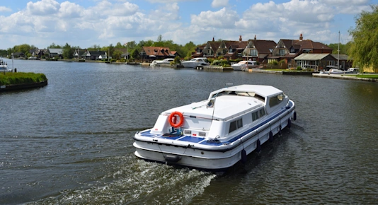 A boat cruising along the River Bure at Horning on the Norfolk Broads, England, UK