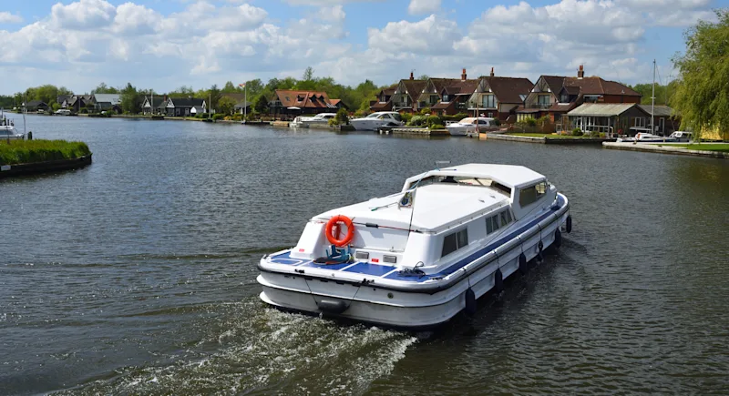A boat cruising along the River Bure at Horning on the Norfolk Broads, England, UK