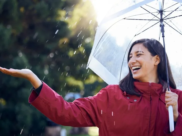 Umbrella, rain and woman with smile, touch and carefree in weather of Seattle, travel and explore in vacation. Park, water and girl in raincoat, outdoor and happy in winter, insurance cover and fun