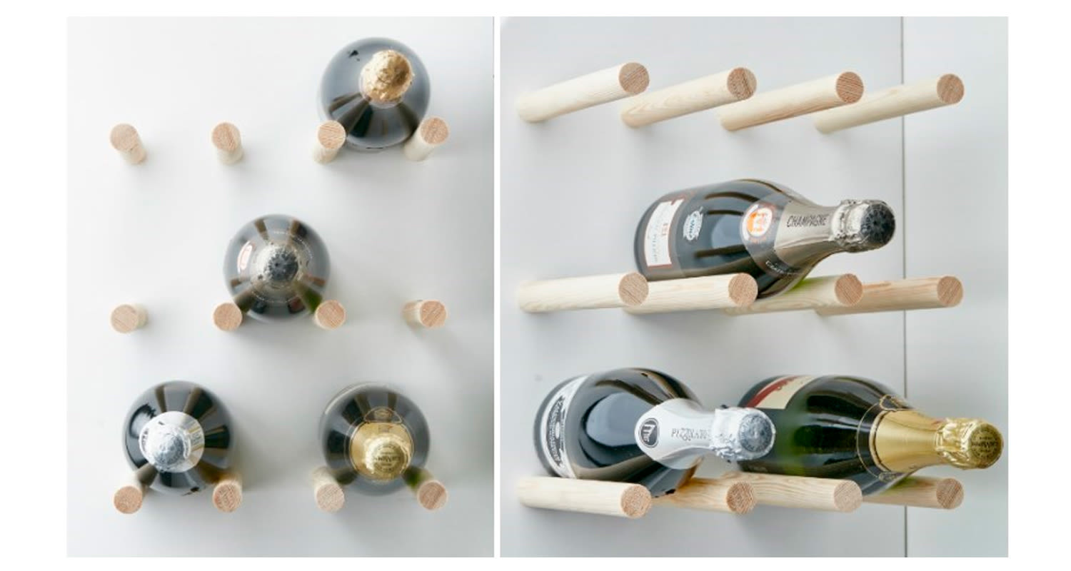 Valkoisella seinällä vaaleat puiset tapit kannattelevat tummia samppanja- ja viinipulloja
