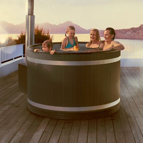 Nelihenkinen perhe porealtaassa puuterassilla järven ja vuorten edessä auringonlaskussa.